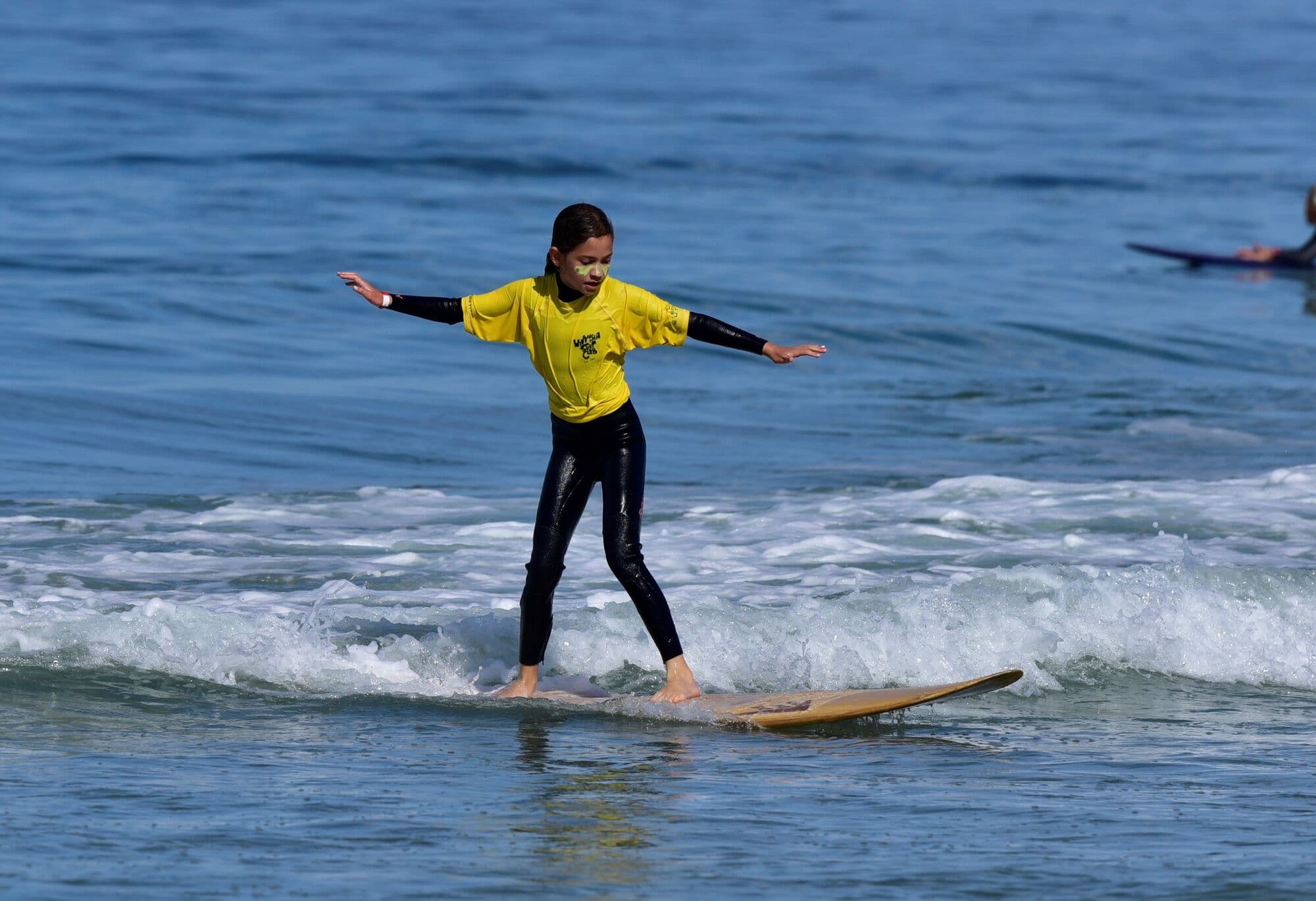 A grom in a yellow jersey riding a longboard with arms out