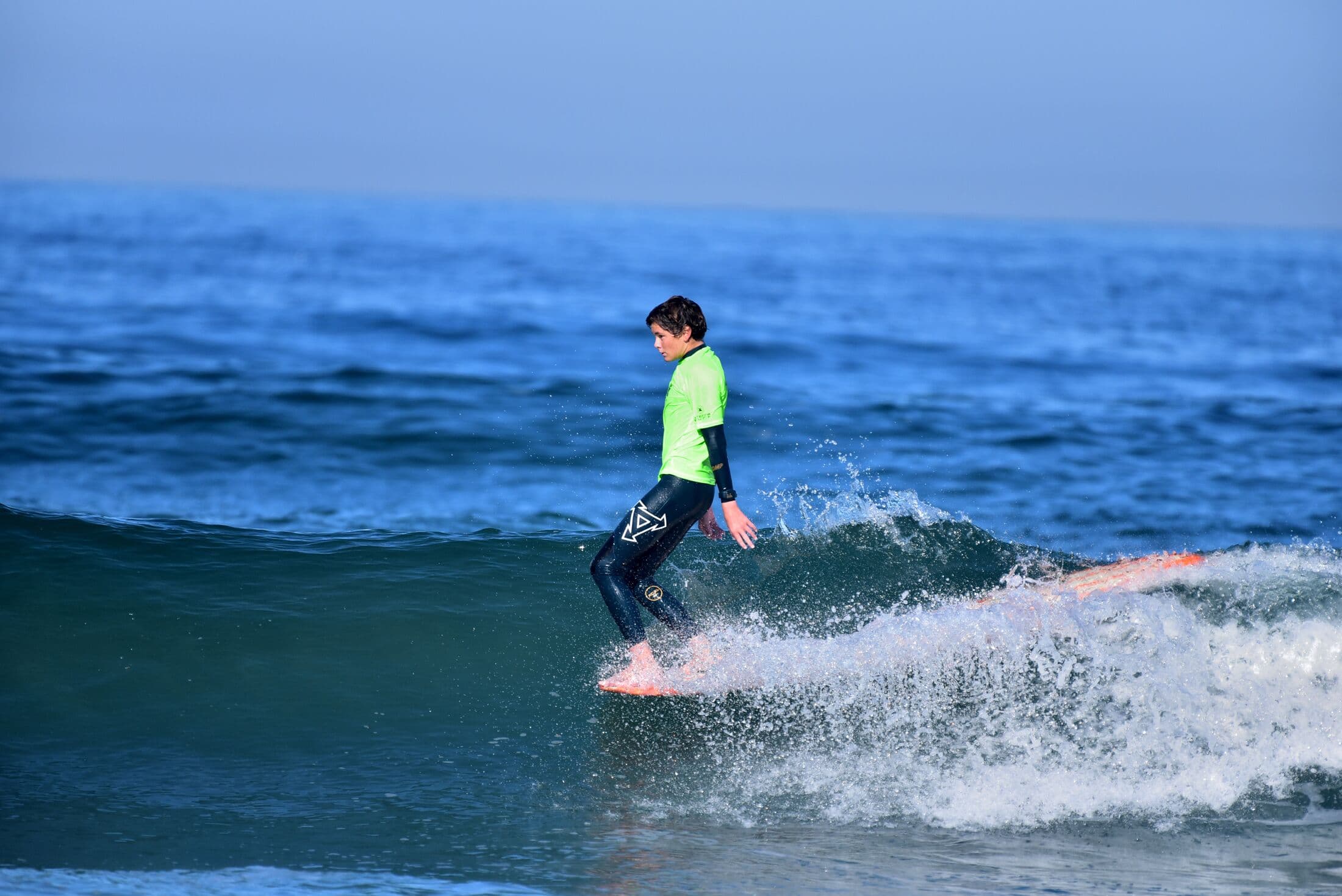 A grom in a green jersey riding a wave